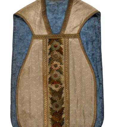 Zdjęcie nr 1: Boki ornatu z białej tkaniny wiskozowej, żakardowej. Wzór o kompozycji rzędowej z motywem trzech nachodzących na siebie okręgów, zwróconych w prawo lub w lewo i przesuniętymi o połowę szerokości raportu w kolejnych rzędach.
Tylna preteksta z tkaniny półjedwabnej o splocie atłasowym, lansowanej nićmi o oplocie metalowym gładkim i karbowanym oraz nićmi bawełnianymi o splocie rządkowym, całość zabezpieczona ściegiem łańcuszkowym. Kompozycja złożona z dwóch przeplatających się wici; złota ze stylizowanymi strzępiastymi liśćmi i wolutowo wygiętymi witkami, żółto-zielona z liśćmi i owocami winnego krzewu. Na przecięciu ramion krzyża preteksty medalion z wizerunkiem Matki Boskiej Apokaliptycznej. Przednia preteksta haftowana na kanwie ściegiem liczonym nićmi bawełnianymi i wełną; na białym tle główki kwiatów w otoczeniu strzępiastych liści, ułożone wertykalnie, w zimnych odcieniach zieleni, brązu i szarości. 
Galony tkane z nićmi o oplocie miedzianym w wątku, w dwóch szerokościach, z motywem zygzaka, jeden lub dwa brzegi ząbkowane.
Podszewka z tkaniny wiskozowej, żakardowej, w kolorze niebieskim. Wzór o kompozycji pasowej z motywem geometrycznym oraz dwóch rodzajów gałązek z kwiatami  i listkami, zwróconymi w prawo lub w lewo i przesuniętymi o połowę szerokości raportu w kolejnych pasach.
