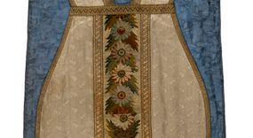 Zdjęcie nr 1: Boki ornatu z białej tkaniny wiskozowej, żakardowej. Wzór o kompozycji rzędowej z motywem trzech nachodzących na siebie okręgów, zwróconych w prawo lub w lewo i przesuniętymi o połowę szerokości raportu w kolejnych rzędach.
Tylna preteksta z tkaniny półjedwabnej o splocie atłasowym, lansowanej nićmi o oplocie metalowym gładkim i karbowanym oraz nićmi bawełnianymi o splocie rządkowym, całość zabezpieczona ściegiem łańcuszkowym. Kompozycja złożona z dwóch przeplatających się wici; złota ze stylizowanymi strzępiastymi liśćmi i wolutowo wygiętymi witkami, żółto-zielona z liśćmi i owocami winnego krzewu. Na przecięciu ramion krzyża preteksty medalion z wizerunkiem Matki Boskiej Apokaliptycznej. Przednia preteksta haftowana na kanwie ściegiem liczonym nićmi bawełnianymi i wełną; na białym tle główki kwiatów w otoczeniu strzępiastych liści, ułożone wertykalnie, w zimnych odcieniach zieleni, brązu i szarości. 
Galony tkane z nićmi o oplocie miedzianym w wątku, w dwóch szerokościach, z motywem zygzaka, jeden lub dwa brzegi ząbkowane.
Podszewka z tkaniny wiskozowej, żakardowej, w kolorze niebieskim. Wzór o kompozycji pasowej z motywem geometrycznym oraz dwóch rodzajów gałązek z kwiatami  i listkami, zwróconymi w prawo lub w lewo i przesuniętymi o połowę szerokości raportu w kolejnych pasach.
