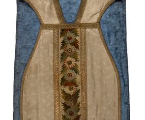 Zdjęcie nr 1: Boki ornatu z białej tkaniny wiskozowej, żakardowej. Wzór o kompozycji rzędowej z motywem trzech nachodzących na siebie okręgów, zwróconych w prawo lub w lewo i przesuniętymi o połowę szerokości raportu w kolejnych rzędach.
Tylna preteksta z tkaniny półjedwabnej o splocie atłasowym, lansowanej nićmi o oplocie metalowym gładkim i karbowanym oraz nićmi bawełnianymi o splocie rządkowym, całość zabezpieczona ściegiem łańcuszkowym. Kompozycja złożona z dwóch przeplatających się wici; złota ze stylizowanymi strzępiastymi liśćmi i wolutowo wygiętymi witkami, żółto-zielona z liśćmi i owocami winnego krzewu. Na przecięciu ramion krzyża preteksty medalion z wizerunkiem Matki Boskiej Apokaliptycznej. Przednia preteksta haftowana na kanwie ściegiem liczonym nićmi bawełnianymi i wełną; na białym tle główki kwiatów w otoczeniu strzępiastych liści, ułożone wertykalnie, w zimnych odcieniach zieleni, brązu i szarości. 
Galony tkane z nićmi o oplocie miedzianym w wątku, w dwóch szerokościach, z motywem zygzaka, jeden lub dwa brzegi ząbkowane.
Podszewka z tkaniny wiskozowej, żakardowej, w kolorze niebieskim. Wzór o kompozycji pasowej z motywem geometrycznym oraz dwóch rodzajów gałązek z kwiatami  i listkami, zwróconymi w prawo lub w lewo i przesuniętymi o połowę szerokości raportu w kolejnych pasach.
