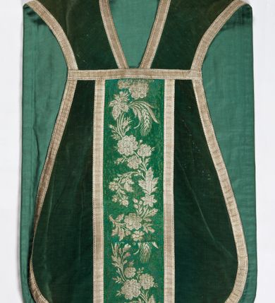 Zdjęcie nr 1: Boki ornatu z zielonego aksamitu bawełnianego.
Preteksty z zielono-srebrnej borty liturgicznej, z jedwabno-bawełnianej, lansowanej nicią o oplocie srebrnym, miejscami wprowadzone bawełniane wątki lansujące w kolorze brązowym, tło z subornamentem o motywach roślinnych. Wzór z motywem esowato wygiętej wici z kwiatów róży, drobnych polnych kwiatów i kłosów zboża. Na przecięciu ramion krzyża tylnej preteksty litery IHS z krzyżem łacińskim otoczone koroną cierniową. Tło przeszyte ściegiem maszynowym w sposób nieregularny.
Galon tkany z nićmi o oplocie miedzianym srebrzonym w wątku i lamelką wzdłuż osnowy w kolorze srebrnym, brzegi z ząbkami.
Podszewka z tkaniny bawełnianej o splocie rządkowym, w kolorze zielonym.
