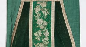 Zdjęcie nr 1: Boki ornatu z zielonego aksamitu bawełnianego.
Preteksty z zielono-srebrnej borty liturgicznej, z jedwabno-bawełnianej, lansowanej nicią o oplocie srebrnym, miejscami wprowadzone bawełniane wątki lansujące w kolorze brązowym, tło z subornamentem o motywach roślinnych. Wzór z motywem esowato wygiętej wici z kwiatów róży, drobnych polnych kwiatów i kłosów zboża. Na przecięciu ramion krzyża tylnej preteksty litery IHS z krzyżem łacińskim otoczone koroną cierniową. Tło przeszyte ściegiem maszynowym w sposób nieregularny.
Galon tkany z nićmi o oplocie miedzianym srebrzonym w wątku i lamelką wzdłuż osnowy w kolorze srebrnym, brzegi z ząbkami.
Podszewka z tkaniny bawełnianej o splocie rządkowym, w kolorze zielonym.
