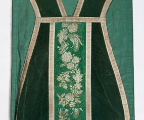 Zdjęcie nr 1: Boki ornatu z zielonego aksamitu bawełnianego.
Preteksty z zielono-srebrnej borty liturgicznej, z jedwabno-bawełnianej, lansowanej nicią o oplocie srebrnym, miejscami wprowadzone bawełniane wątki lansujące w kolorze brązowym, tło z subornamentem o motywach roślinnych. Wzór z motywem esowato wygiętej wici z kwiatów róży, drobnych polnych kwiatów i kłosów zboża. Na przecięciu ramion krzyża tylnej preteksty litery IHS z krzyżem łacińskim otoczone koroną cierniową. Tło przeszyte ściegiem maszynowym w sposób nieregularny.
Galon tkany z nićmi o oplocie miedzianym srebrzonym w wątku i lamelką wzdłuż osnowy w kolorze srebrnym, brzegi z ząbkami.
Podszewka z tkaniny bawełnianej o splocie rządkowym, w kolorze zielonym.
