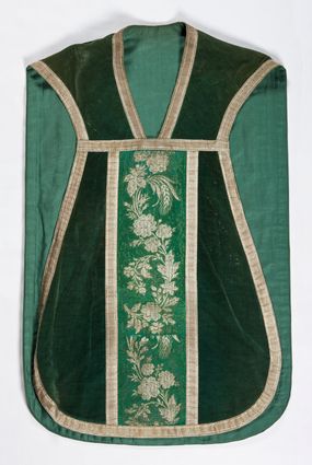 Zdjęcie nr 1: Boki ornatu z zielonego aksamitu bawełnianego.
Preteksty z zielono-srebrnej borty liturgicznej, z jedwabno-bawełnianej, lansowanej nicią o oplocie srebrnym, miejscami wprowadzone bawełniane wątki lansujące w kolorze brązowym, tło z subornamentem o motywach roślinnych. Wzór z motywem esowato wygiętej wici z kwiatów róży, drobnych polnych kwiatów i kłosów zboża. Na przecięciu ramion krzyża tylnej preteksty litery IHS z krzyżem łacińskim otoczone koroną cierniową. Tło przeszyte ściegiem maszynowym w sposób nieregularny.
Galon tkany z nićmi o oplocie miedzianym srebrzonym w wątku i lamelką wzdłuż osnowy w kolorze srebrnym, brzegi z ząbkami.
Podszewka z tkaniny bawełnianej o splocie rządkowym, w kolorze zielonym.
