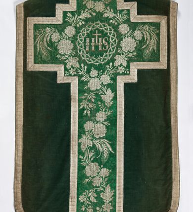 Zdjęcie nr 2: Boki ornatu z zielonego aksamitu bawełnianego.
Preteksty z zielono-srebrnej borty liturgicznej, z jedwabno-bawełnianej, lansowanej nicią o oplocie srebrnym, miejscami wprowadzone bawełniane wątki lansujące w kolorze brązowym, tło z subornamentem o motywach roślinnych. Wzór z motywem esowato wygiętej wici z kwiatów róży, drobnych polnych kwiatów i kłosów zboża. Na przecięciu ramion krzyża tylnej preteksty litery IHS z krzyżem łacińskim otoczone koroną cierniową. Tło przeszyte ściegiem maszynowym w sposób nieregularny.
Galon tkany z nićmi o oplocie miedzianym srebrzonym w wątku i lamelką wzdłuż osnowy w kolorze srebrnym, brzegi z ząbkami.
Podszewka z tkaniny bawełnianej o splocie rządkowym, w kolorze zielonym.
