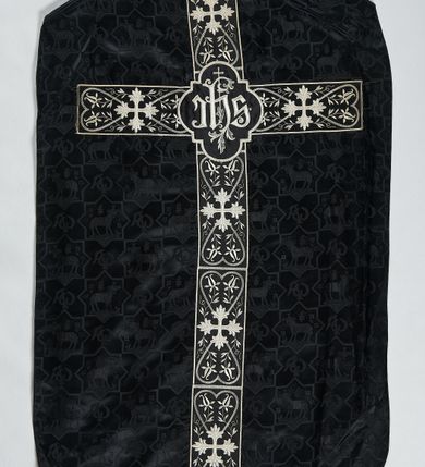 Zdjęcie nr 2: Ornat z czarnej tkaniny wiskozowej, żakardowej, z efektem adamaszku. Wzór o kompozycji sieciowej złożony z pól w kształcie gwiazdy ośmioramiennej (rombu opisanego na kwadracie) i czworoliści o płatkach zamkniętych łukiem dwuspadowym. W polach gwiaździstych przedstawienie Baranka w nimbie krzyżowym, wśród roślinności i z motywem chryzmonu. W kolejnych poziomych pasach Baranek zwrócony w prawo lub w lewo. W polu czteroliści splecione litery alfa i omega. 
Preteksty naszyte z tkaniny wiskozowej o splocie rządkowym, z haftem maszynowym nicią wiskozową, z motywem krzyży greckich o ramionach w kształcie liści, umieszczonych pomiędzy dwoma polami w kształcie serca, z wyrastającymi w górę i w dół parami fantazyjnych kwiatów na ulistnionych falistych łodyżkach. Na przecięciu ramion tylnej preteksty krzyżowej medalion w kształcie wydłużonego czworoliścia opisanego na kwadracie, ze stylizowanymi literami IHS z cienkim krzyżykiem łacińskim.
Podszewka z tkaniny syntetycznej o splocie rypsowym, w kolorze czarnym. Na podszewce metka z niebieskim napisem: Made by / THE MADONNA GUILDS / Especially For / Michigan Church Supply Co.