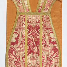 Zdjęcie nr 1: Ornat jednolity z czerwono-białej tkaniny półjedwabnej (?), żakardowej. Wzór o kompozycji sieciowej z motywem drobnych girland kwiatowych, rozłożystych centralnie umieszczonych układów roślinno-kwiatowych i elementów nawiązujących do ornamentu okuciowo-kartuszowego.

Galony tkane z nićmi o oplocie miedzianym złoconym w wątku, w dwóch szerokościach, z motywem czwórlistnych kwiatków i diagonalnych liści, brzegi z ząbkami.

Podszewka z tkaniny wiskozowej o splocie rządkowym, w kolorze pomarańczowym.