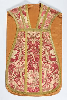 Zdjęcie nr 1: Ornat jednolity z czerwono-białej tkaniny półjedwabnej (?), żakardowej. Wzór o kompozycji sieciowej z motywem drobnych girland kwiatowych, rozłożystych centralnie umieszczonych układów roślinno-kwiatowych i elementów nawiązujących do ornamentu okuciowo-kartuszowego.

Galony tkane z nićmi o oplocie miedzianym złoconym w wątku, w dwóch szerokościach, z motywem czwórlistnych kwiatków i diagonalnych liści, brzegi z ząbkami.

Podszewka z tkaniny wiskozowej o splocie rządkowym, w kolorze pomarańczowym.