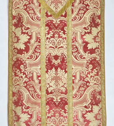 Zdjęcie nr 2: Ornat jednolity z czerwono-białej tkaniny półjedwabnej (?), żakardowej. Wzór o kompozycji sieciowej z motywem drobnych girland kwiatowych, rozłożystych centralnie umieszczonych układów roślinno-kwiatowych i elementów nawiązujących do ornamentu okuciowo-kartuszowego.

Galony tkane z nićmi o oplocie miedzianym złoconym w wątku, w dwóch szerokościach, z motywem czwórlistnych kwiatków i diagonalnych liści, brzegi z ząbkami.

Podszewka z tkaniny wiskozowej o splocie rządkowym, w kolorze pomarańczowym.