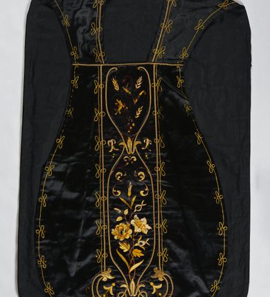 Zdjęcie nr 1: Ornat z czarnej tkaniny półjedwabnej o splocie atłasowym.

Preteksty wyznaczone haftem barwnym, ściegiem łańcuszkowym maszynowym nićmi sztucznymi, uzupełnione haftem kładzionym z sutaszem o oplocie miedzianym złoconym oraz haftem na podkładzie tekturowym nićmi gładkimi i karbowanymi o oplocie miedzianym złoconym. Kompozycja roślinno-kwiatowa zamknięta pomiędzy dwoma wiciami fantazyjnie wygiętymi na zakończeniach, z motywami lilii andegaweńskich, w kolorze złotym oraz gałązek winnej latorośli z gronami, kłosami zboża i gałązkami kwiatu róży i lilii, w odcieniach brązu. Na przecięciu ramion tylnej preteksty litery IHS z krzyżem łacińskim i gwoźdźmi, w kolorze złotym. Całość otacza dekoracyjny fryz w kolorze żółtym.

Podszewka z tkaniny bawełnianej o splocie rządkowym, w kolorze czarnym. Na podszewce metka w kolorze białym, z jasnoniebieskim napisem: "Made in France/The C. Wildermann Co/NEW - YORK".
