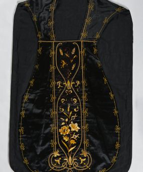 Zdjęcie nr 1: Ornat z czarnej tkaniny półjedwabnej o splocie atłasowym.

Preteksty wyznaczone haftem barwnym, ściegiem łańcuszkowym maszynowym nićmi sztucznymi, uzupełnione haftem kładzionym z sutaszem o oplocie miedzianym złoconym oraz haftem na podkładzie tekturowym nićmi gładkimi i karbowanymi o oplocie miedzianym złoconym. Kompozycja roślinno-kwiatowa zamknięta pomiędzy dwoma wiciami fantazyjnie wygiętymi na zakończeniach, z motywami lilii andegaweńskich, w kolorze złotym oraz gałązek winnej latorośli z gronami, kłosami zboża i gałązkami kwiatu róży i lilii, w odcieniach brązu. Na przecięciu ramion tylnej preteksty litery IHS z krzyżem łacińskim i gwoźdźmi, w kolorze złotym. Całość otacza dekoracyjny fryz w kolorze żółtym.

Podszewka z tkaniny bawełnianej o splocie rządkowym, w kolorze czarnym. Na podszewce metka w kolorze białym, z jasnoniebieskim napisem: "Made in France/The C. Wildermann Co/NEW - YORK".