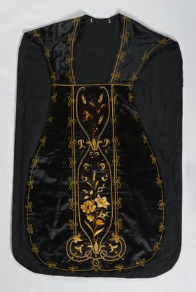 Zdjęcie nr 1: Ornat z czarnej tkaniny półjedwabnej o splocie atłasowym.

Preteksty wyznaczone haftem barwnym, ściegiem łańcuszkowym maszynowym nićmi sztucznymi, uzupełnione haftem kładzionym z sutaszem o oplocie miedzianym złoconym oraz haftem na podkładzie tekturowym nićmi gładkimi i karbowanymi o oplocie miedzianym złoconym. Kompozycja roślinno-kwiatowa zamknięta pomiędzy dwoma wiciami fantazyjnie wygiętymi na zakończeniach, z motywami lilii andegaweńskich, w kolorze złotym oraz gałązek winnej latorośli z gronami, kłosami zboża i gałązkami kwiatu róży i lilii, w odcieniach brązu. Na przecięciu ramion tylnej preteksty litery IHS z krzyżem łacińskim i gwoźdźmi, w kolorze złotym. Całość otacza dekoracyjny fryz w kolorze żółtym.

Podszewka z tkaniny bawełnianej o splocie rządkowym, w kolorze czarnym. Na podszewce metka w kolorze białym, z jasnoniebieskim napisem: "Made in France/The C. Wildermann Co/NEW - YORK".