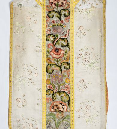 Zdjęcie nr 2: Boki ornatu z białej tkaniny wiskozowej o splocie rypsowym z malowanym wzorem z motywów okazałych bukietów drobnych kwiatów przewiązanych kokardą i mniejszych gałązek kwiatowych. W górnej części ornatu, na wysokości ramion, tkanina wiskozowa o tle w splocie rypsowym, żakardowa, z wzorem o kompozycji pasowej z ułożonych poziomo bukiecików drobnych kwiatków z listkami i luźno rozrzuconych małych kwiatków.

Preteksty w partii tła założone haftem kładzionym nicią o oplocie metalowym w kolorze srebrnym; wzór haftowany barwnymi nićmi ściegiem cieniowanym,  z motywem gałązek z fantazyjnie wygiętymi liśćmi i barwnymi kwiatami, m.in. róży i goździka. Dolna część tylnej preteksty uzupełniona podobnym haftem.

Galony tkane z nici sztucznych, trójbarwne (tło żółte, wzór biało-czerwony), w dwóch szerokościach i o dwóch wzorach: 1. przy pretekstach szerszy, z motywem białych krzyżyków greckich, motywem w kształcie litery X i rombów z wpisanym małym krzyżykiem, wszystkie z czerwonymi środkami; 2. na brzegach, z motywem białych krzyżyków greckich i ośmiopłatkowych kwiatków, z czerwonymi środkami i przedzielone czerwonymi kostkami. U dołu przedniej preteksty wstawiony fragment galonu tkanego z nićmi o oplocie miedzianym srebrzonym w wątku, z motywem falistej prążkowanej wstęgi i trójklapowych listków.

Podszewka z tkaniny wiskozowej o splocie rządkowym, w kolorze pomarańczowym.