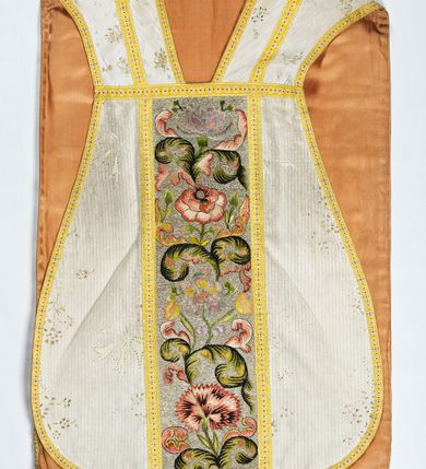 Zdjęcie nr 1: Boki ornatu z białej tkaniny wiskozowej o splocie rypsowym z malowanym wzorem z motywów okazałych bukietów drobnych kwiatów przewiązanych kokardą i mniejszych gałązek kwiatowych. W górnej części ornatu, na wysokości ramion, tkanina wiskozowa o tle w splocie rypsowym, żakardowa, z wzorem o kompozycji pasowej z ułożonych poziomo bukiecików drobnych kwiatków z listkami i luźno rozrzuconych małych kwiatków.

Preteksty w partii tła założone haftem kładzionym nicią o oplocie metalowym w kolorze srebrnym; wzór haftowany barwnymi nićmi ściegiem cieniowanym,  z motywem gałązek z fantazyjnie wygiętymi liśćmi i barwnymi kwiatami, m.in. róży i goździka. Dolna część tylnej preteksty uzupełniona podobnym haftem.

Galony tkane z nici sztucznych, trójbarwne (tło żółte, wzór biało-czerwony), w dwóch szerokościach i o dwóch wzorach: 1. przy pretekstach szerszy, z motywem białych krzyżyków greckich, motywem w kształcie litery X i rombów z wpisanym małym krzyżykiem, wszystkie z czerwonymi środkami; 2. na brzegach, z motywem białych krzyżyków greckich i ośmiopłatkowych kwiatków, z czerwonymi środkami i przedzielone czerwonymi kostkami. U dołu przedniej preteksty wstawiony fragment galonu tkanego z nićmi o oplocie miedzianym srebrzonym w wątku, z motywem falistej prążkowanej wstęgi i trójklapowych listków.

Podszewka z tkaniny wiskozowej o splocie rządkowym, w kolorze pomarańczowym.