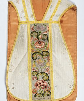 Zdjęcie nr 1: Boki ornatu z białej tkaniny wiskozowej o splocie rypsowym z malowanym wzorem z motywów okazałych bukietów drobnych kwiatów przewiązanych kokardą i mniejszych gałązek kwiatowych. W górnej części ornatu, na wysokości ramion, tkanina wiskozowa o tle w splocie rypsowym, żakardowa, z wzorem o kompozycji pasowej z ułożonych poziomo bukiecików drobnych kwiatków z listkami i luźno rozrzuconych małych kwiatków.

Preteksty w partii tła założone haftem kładzionym nicią o oplocie metalowym w kolorze srebrnym; wzór haftowany barwnymi nićmi ściegiem cieniowanym,  z motywem gałązek z fantazyjnie wygiętymi liśćmi i barwnymi kwiatami, m.in. róży i goździka. Dolna część tylnej preteksty uzupełniona podobnym haftem.

Galony tkane z nici sztucznych, trójbarwne (tło żółte, wzór biało-czerwony), w dwóch szerokościach i o dwóch wzorach: 1. przy pretekstach szerszy, z motywem białych krzyżyków greckich, motywem w kształcie litery X i rombów z wpisanym małym krzyżykiem, wszystkie z czerwonymi środkami; 2. na brzegach, z motywem białych krzyżyków greckich i ośmiopłatkowych kwiatków, z czerwonymi środkami i przedzielone czerwonymi kostkami. U dołu przedniej preteksty wstawiony fragment galonu tkanego z nićmi o oplocie miedzianym srebrzonym w wątku, z motywem falistej prążkowanej wstęgi i trójklapowych listków.

Podszewka z tkaniny wiskozowej o splocie rządkowym, w kolorze pomarańczowym.