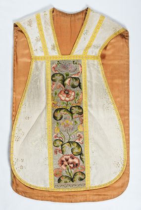 Zdjęcie nr 1: Boki ornatu z białej tkaniny wiskozowej o splocie rypsowym z malowanym wzorem z motywów okazałych bukietów drobnych kwiatów przewiązanych kokardą i mniejszych gałązek kwiatowych. W górnej części ornatu, na wysokości ramion, tkanina wiskozowa o tle w splocie rypsowym, żakardowa, z wzorem o kompozycji pasowej z ułożonych poziomo bukiecików drobnych kwiatków z listkami i luźno rozrzuconych małych kwiatków.

Preteksty w partii tła założone haftem kładzionym nicią o oplocie metalowym w kolorze srebrnym; wzór haftowany barwnymi nićmi ściegiem cieniowanym,  z motywem gałązek z fantazyjnie wygiętymi liśćmi i barwnymi kwiatami, m.in. róży i goździka. Dolna część tylnej preteksty uzupełniona podobnym haftem.

Galony tkane z nici sztucznych, trójbarwne (tło żółte, wzór biało-czerwony), w dwóch szerokościach i o dwóch wzorach: 1. przy pretekstach szerszy, z motywem białych krzyżyków greckich, motywem w kształcie litery X i rombów z wpisanym małym krzyżykiem, wszystkie z czerwonymi środkami; 2. na brzegach, z motywem białych krzyżyków greckich i ośmiopłatkowych kwiatków, z czerwonymi środkami i przedzielone czerwonymi kostkami. U dołu przedniej preteksty wstawiony fragment galonu tkanego z nićmi o oplocie miedzianym srebrzonym w wątku, z motywem falistej prążkowanej wstęgi i trójklapowych listków.

Podszewka z tkaniny wiskozowej o splocie rządkowym, w kolorze pomarańczowym.